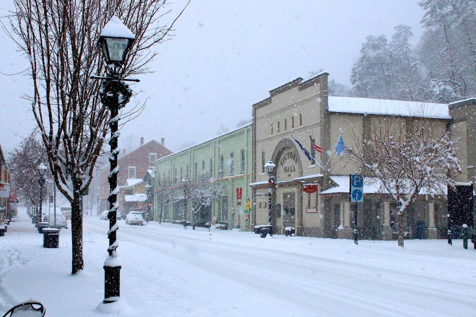 Snow falling on Valley Street in downtown Scottsville, with Victory Hall and a garland-wrapped lamppost