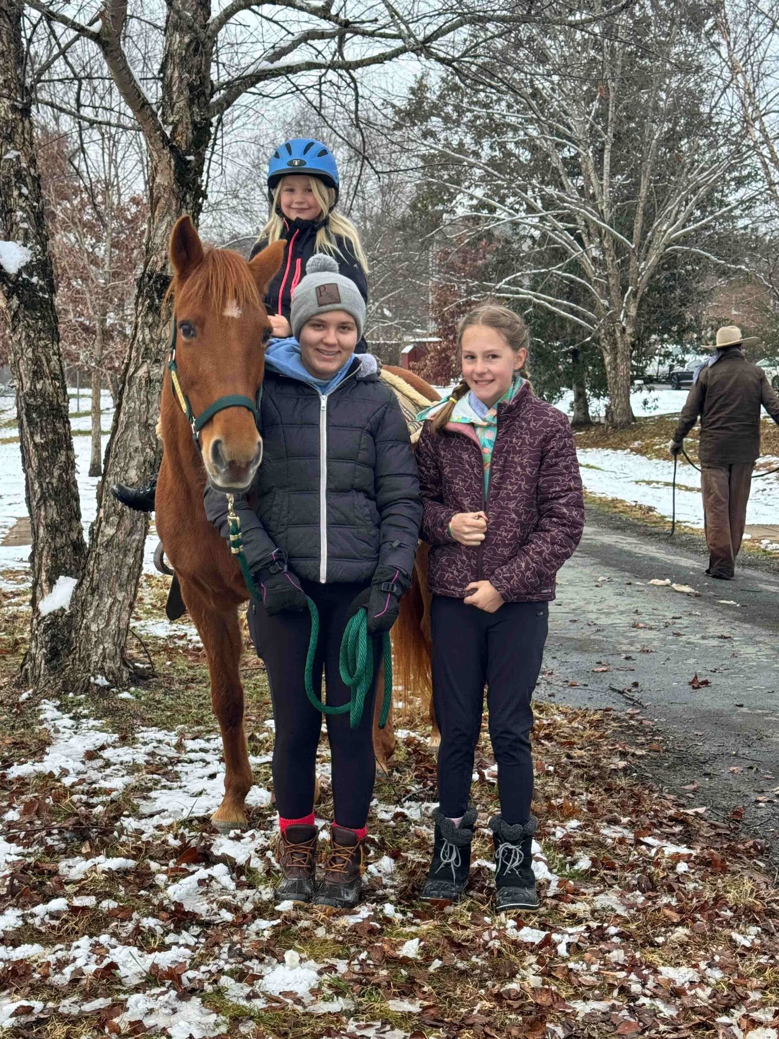 A young rider on a chestnut pony with two girls standing beside it in the snow