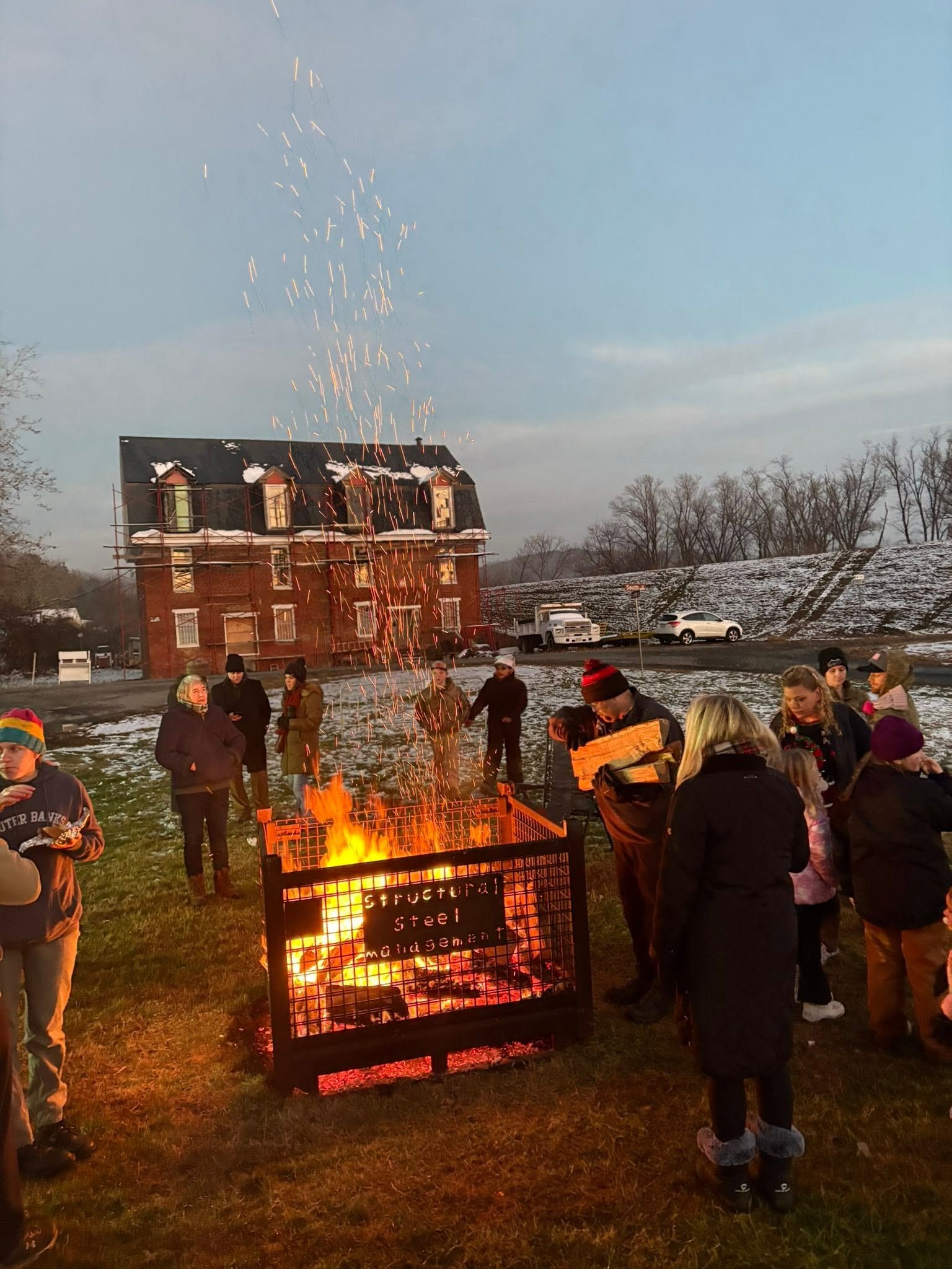 Neighbors gathered around a bonfire as sparks rise into the evening sky
